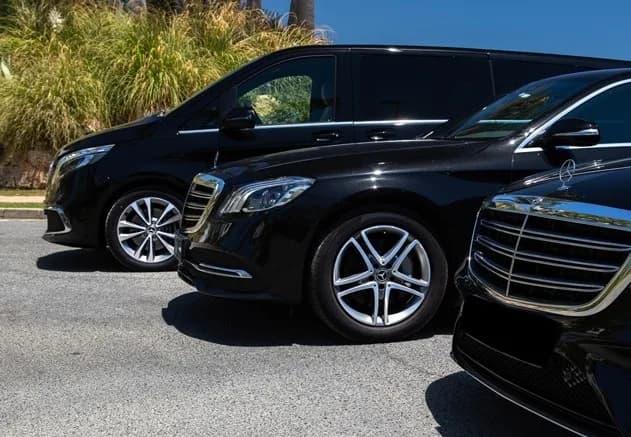 Drie zwarte wagens naast elkaar: twee personenauto's en een taxibus